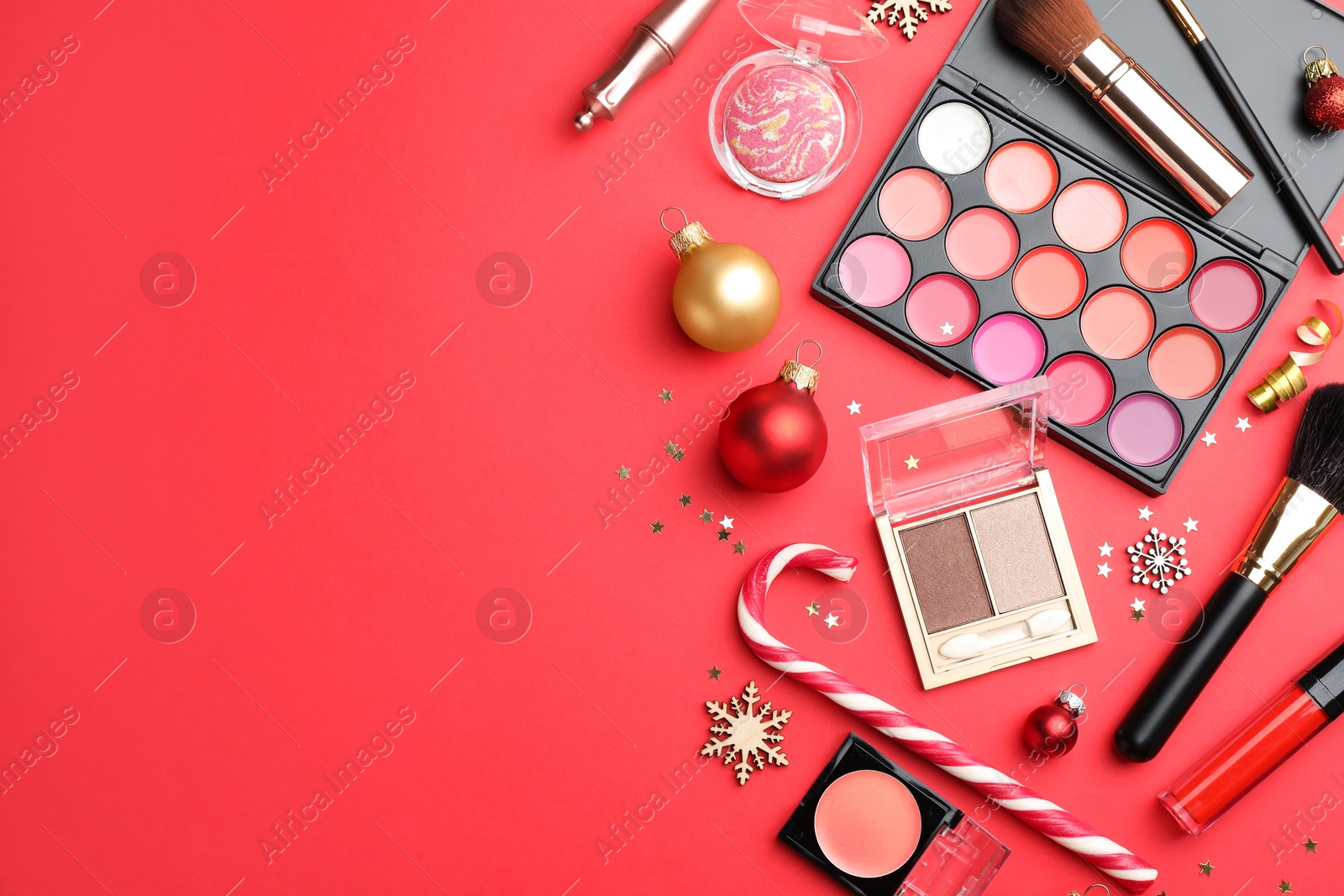 Photo of Flat lay composition with makeup products and Christmas decor on red background. Space for text