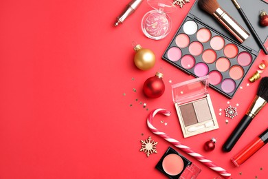 Flat lay composition with makeup products and Christmas decor on red background. Space for text