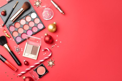 Flat lay composition with makeup products and Christmas decor on red background. Space for text