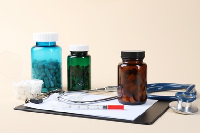 Photo of Pharmacist. Pills in plastic bottles, clipboard, syringe and stethoscope on beige background