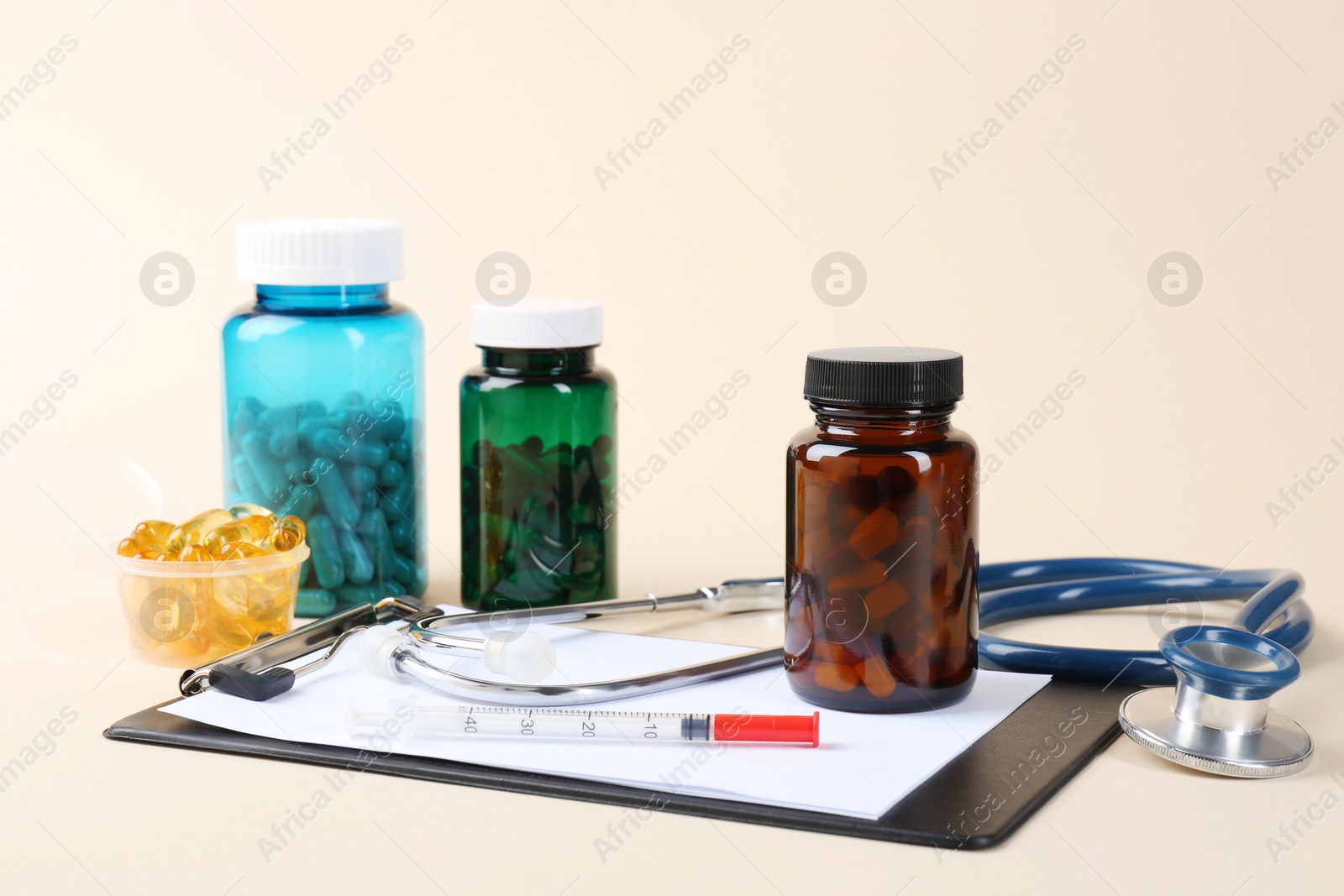 Photo of Pharmacist. Pills in plastic bottles, clipboard, syringe and stethoscope on beige background