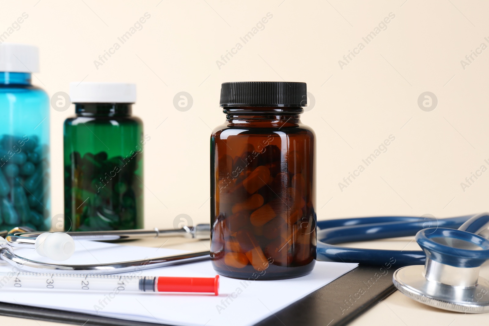 Photo of Pharmacist. Pills in plastic bottles, clipboard, syringe and stethoscope on beige background