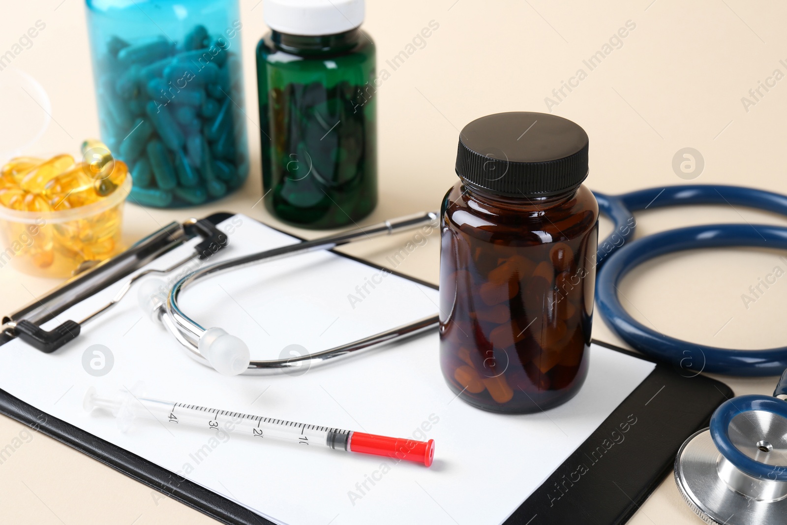 Photo of Pharmacist. Pills in plastic bottles, clipboard, syringe and stethoscope on beige background