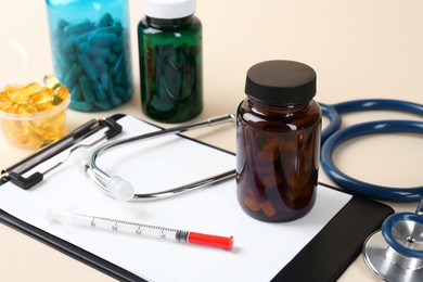 Photo of Pharmacist. Pills in plastic bottles, clipboard, syringe and stethoscope on beige background