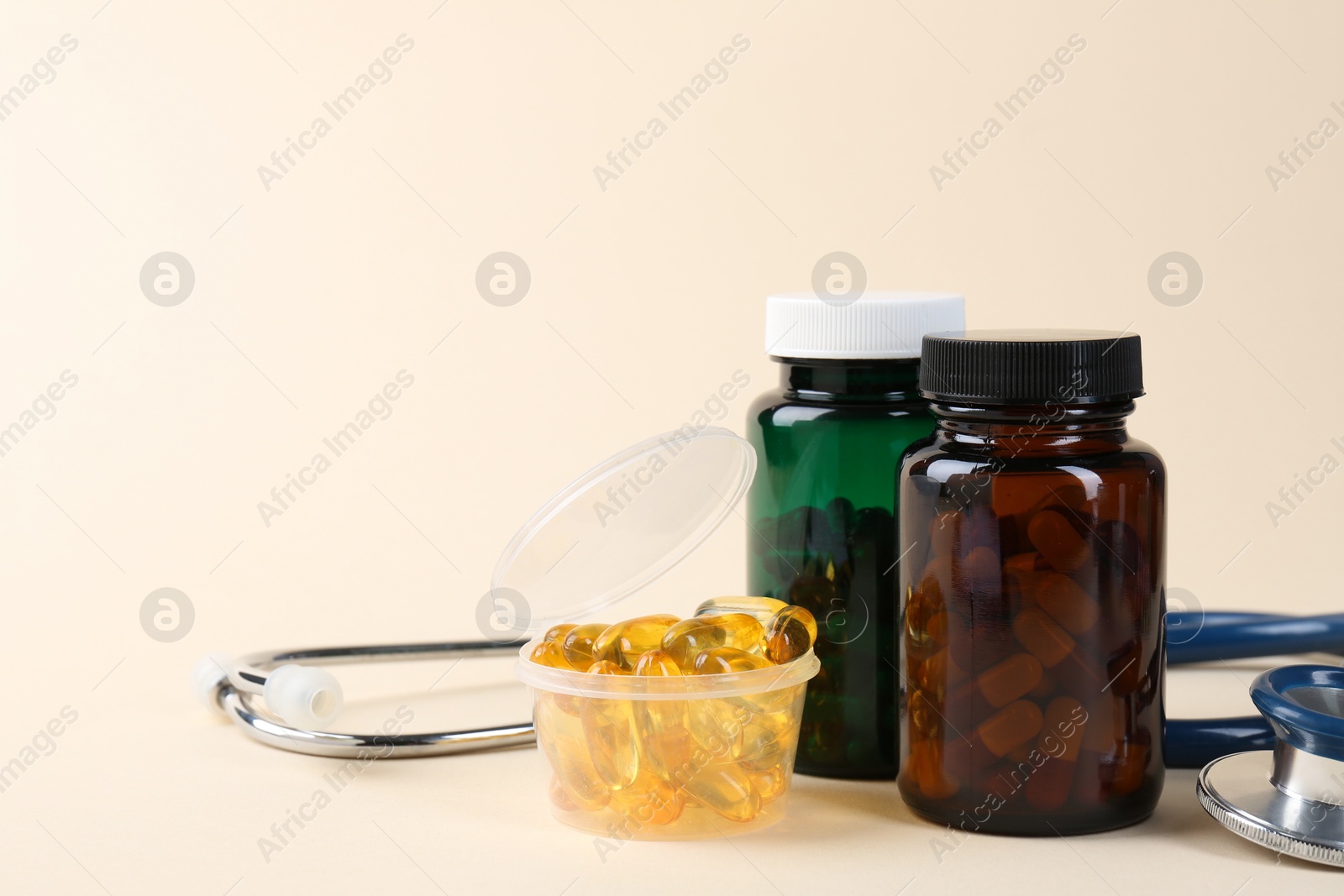 Photo of Pharmacist. Many pills in plastic container, bottles and stethoscope on beige background