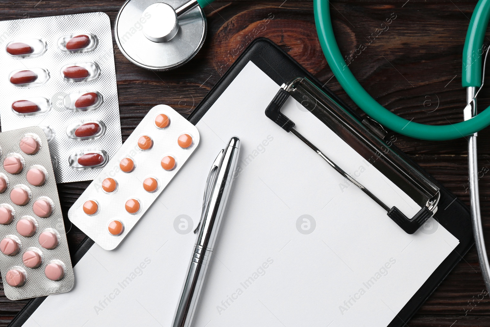 Photo of Pharmacist. Many different pills, clipboard, pen and stethoscope on wooden table, top view