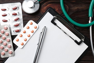 Pharmacist. Many different pills, clipboard, pen and stethoscope on wooden table, top view