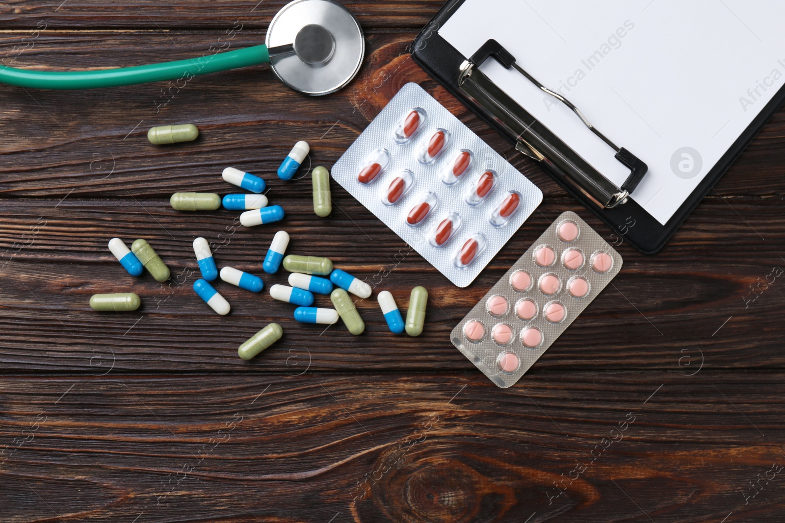 Photo of Pharmacist. Many different pills, clipboard and stethoscope on wooden table, flat lay