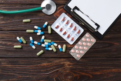 Photo of Pharmacist. Many different pills, clipboard and stethoscope on wooden table, flat lay