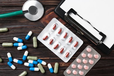 Pharmacist. Many different pills, clipboard and stethoscope on wooden table, flat lay