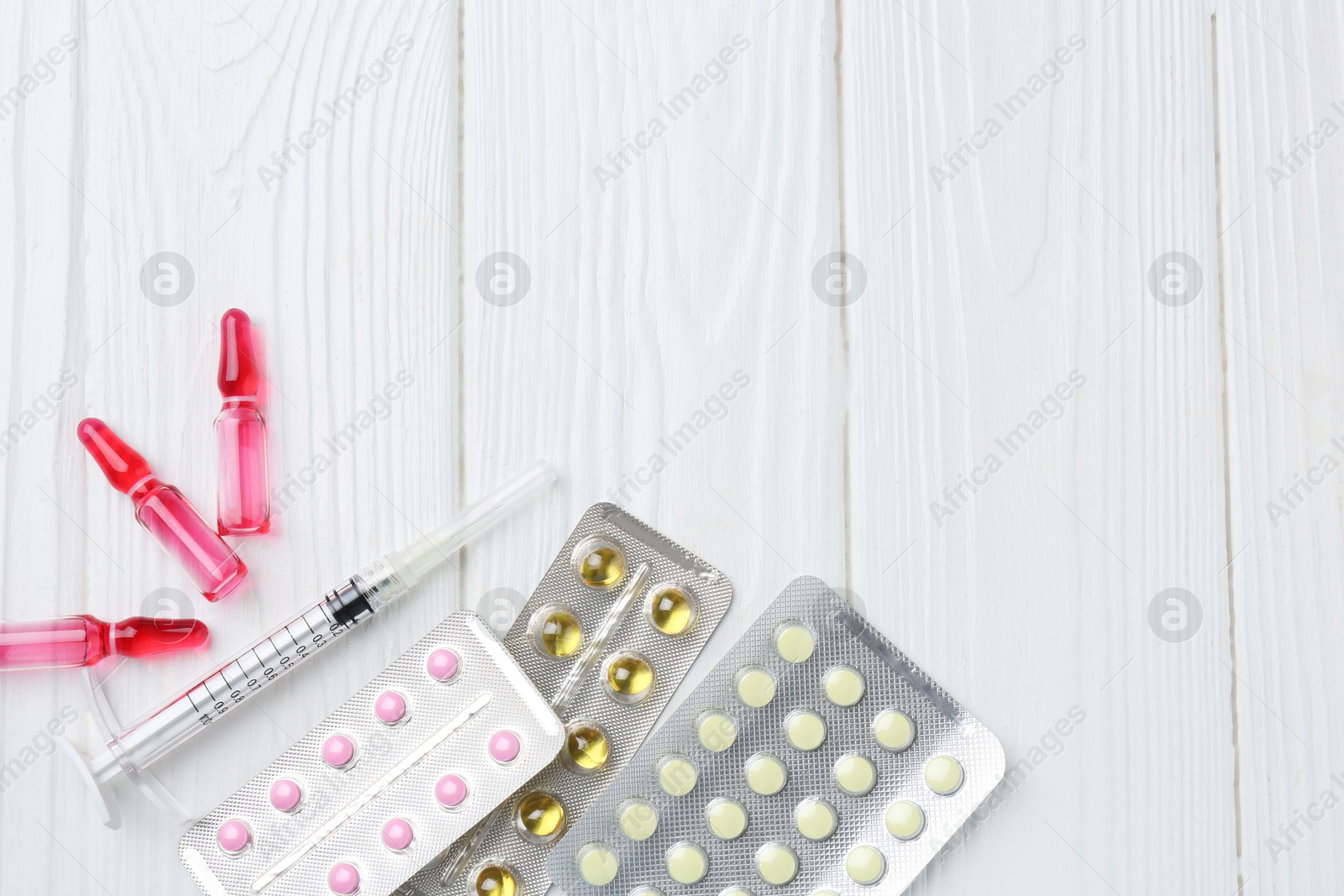 Photo of Pharmacist. Many different pills, syringe and ampoules on white wooden table, flat lay. Space for text