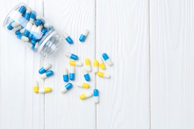 Photo of Pharmacist. Many different pills and overturned bottle on white wooden table, top view. Space for text