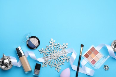 Flat lay composition with makeup products and Christmas decor on light blue background. Space for text