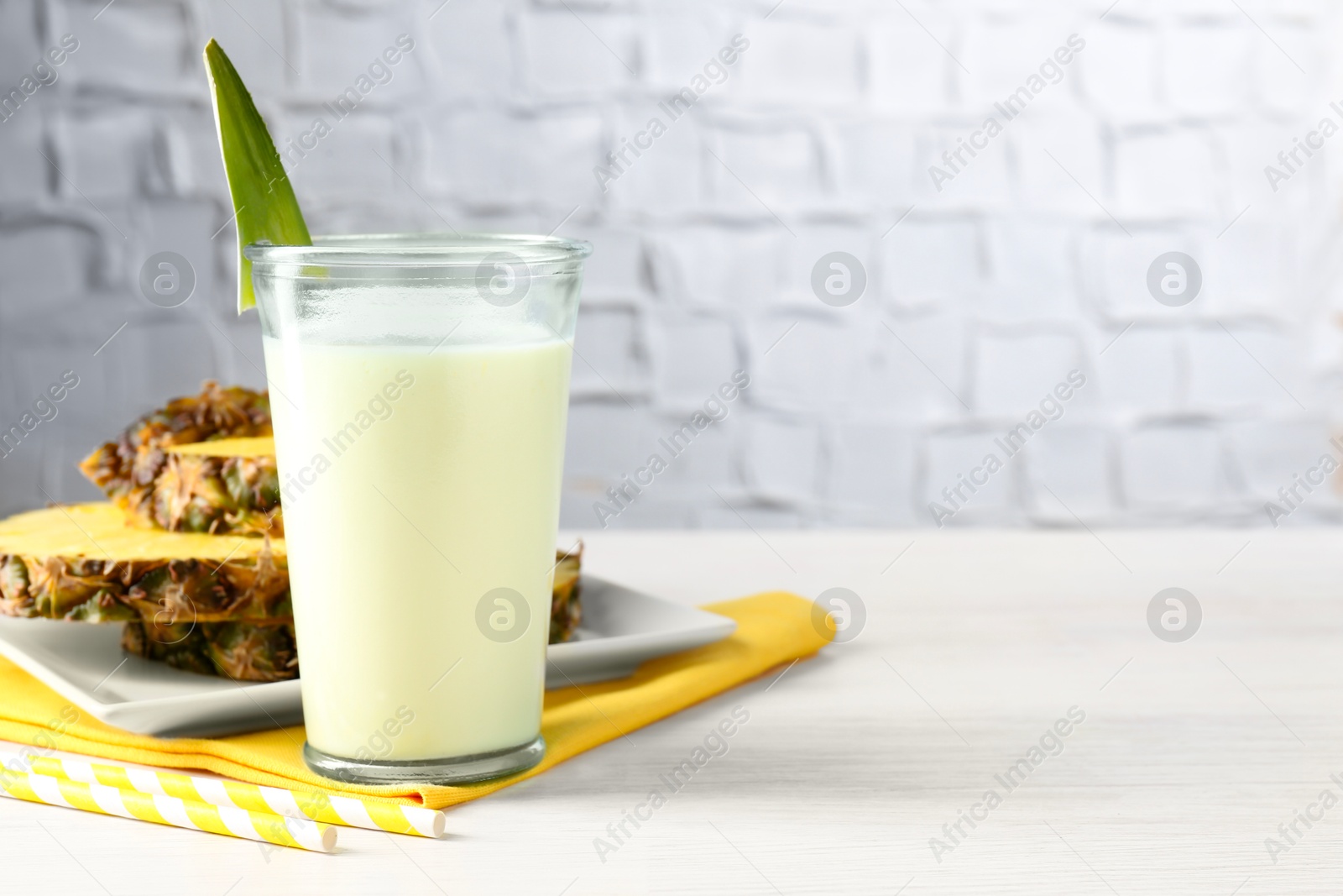 Photo of Tasty pineapple smoothie in glass and fresh fruit on white wooden table, space for text