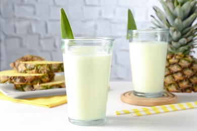 Photo of Tasty pineapple smoothie in glasses and fresh fruit on white wooden table