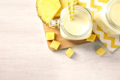 Photo of Tasty pineapple smoothie in mason jars and fresh fruit on white wooden table, top view. Space for text