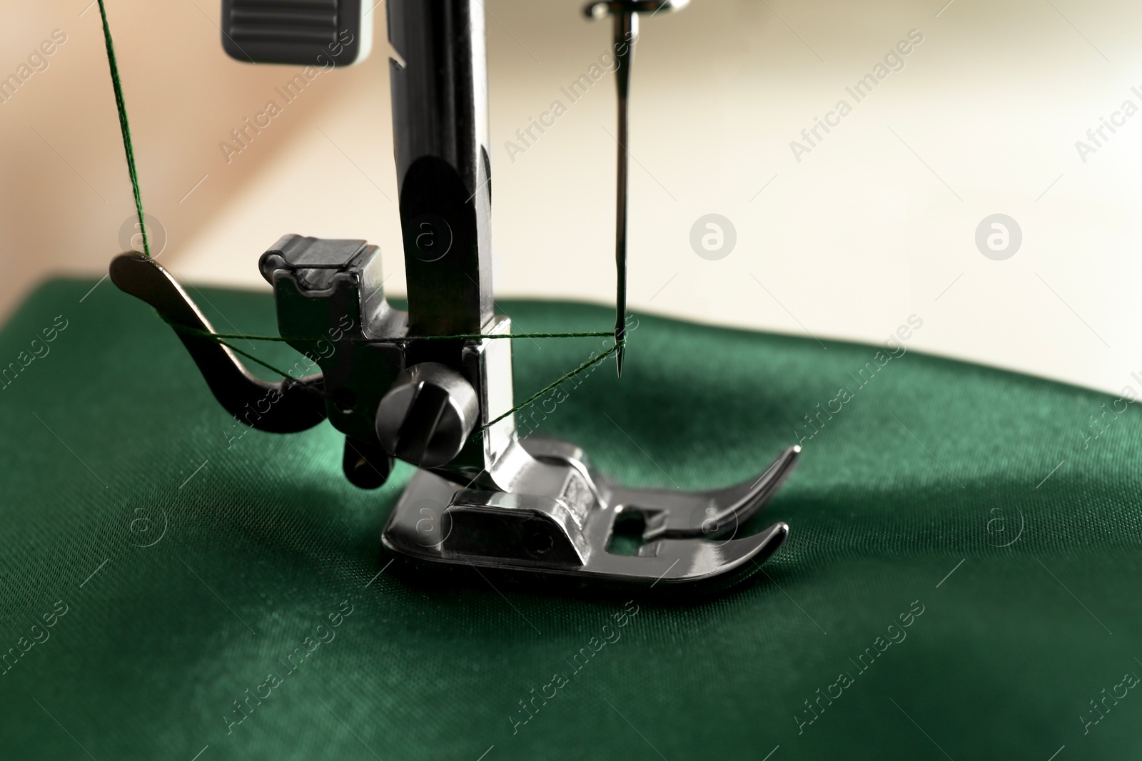 Photo of Sewing machine with green fabric on light background, closeup