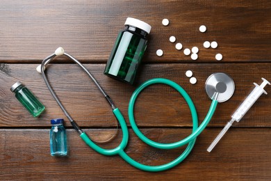 Pharmacist. Many pills, stethoscope, plastic bottle, syringe and glass vials on wooden table, flat lay