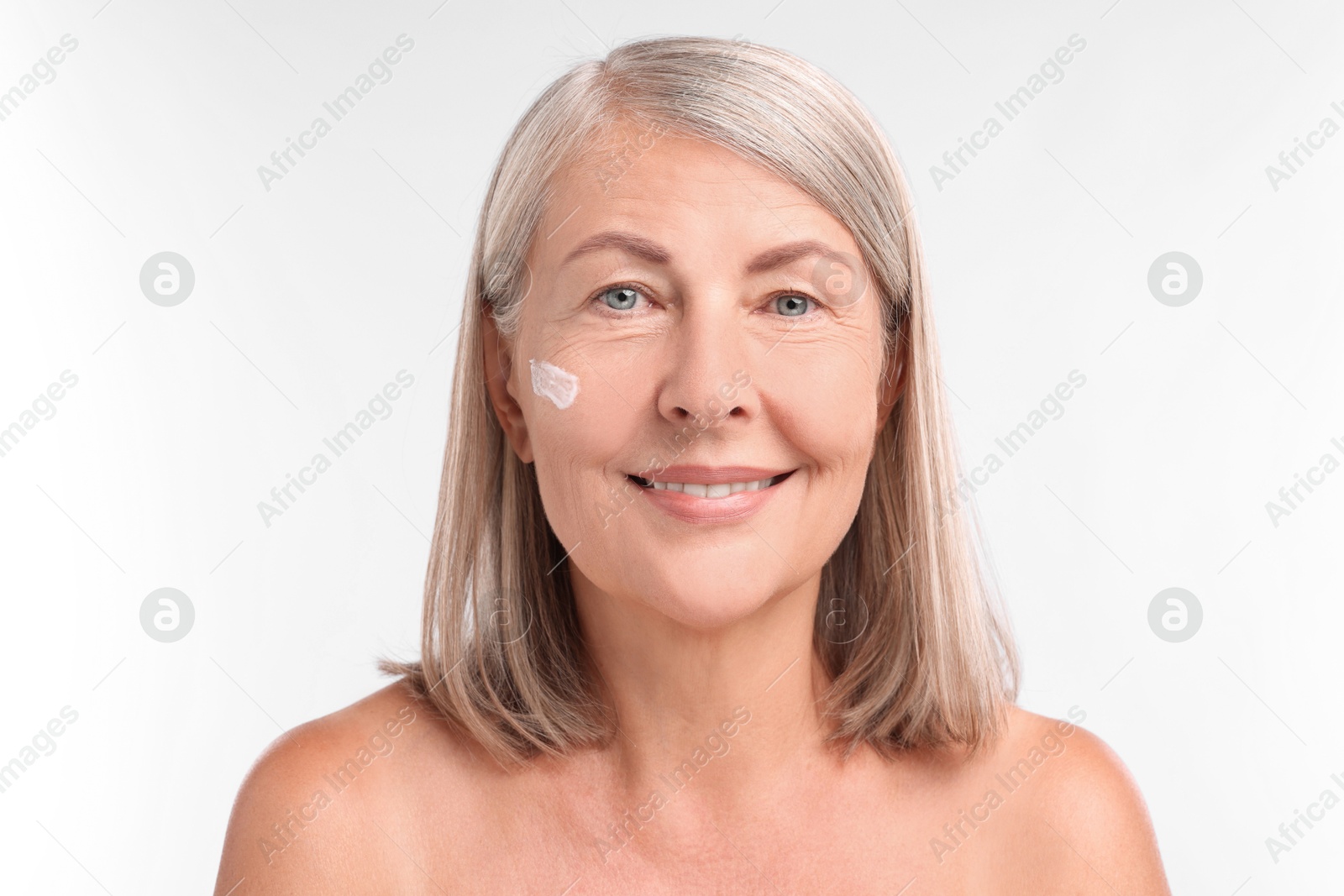 Photo of Senior woman with face cream on white background