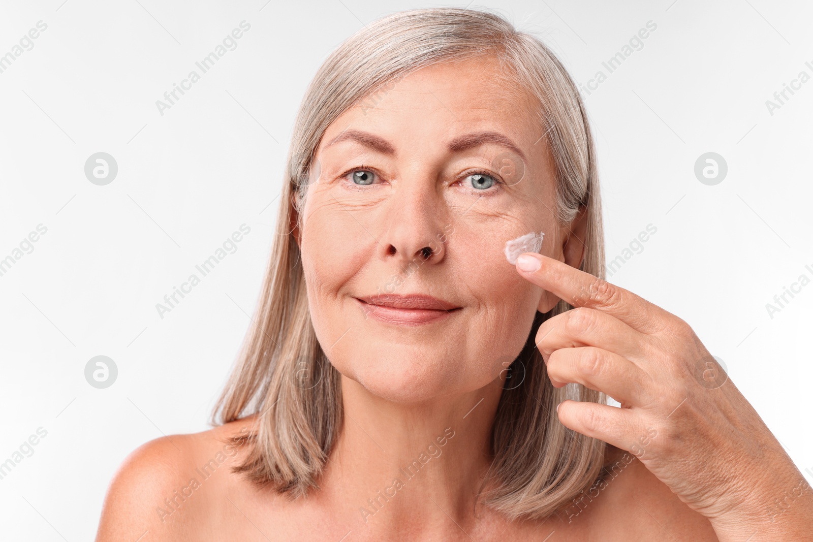 Photo of Senior woman applying face cream on white background