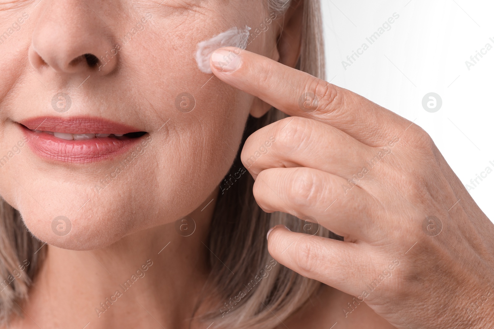 Photo of Senior woman applying face cream on white background, closeup