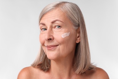 Senior woman with face cream on white background