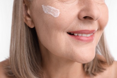 Photo of Senior woman with face cream on white background, closeup