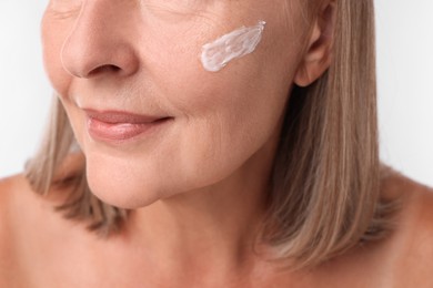 Photo of Senior woman with face cream on white background, closeup