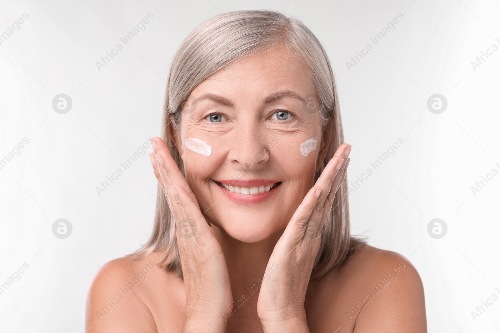 Photo of Senior woman with face cream on white background