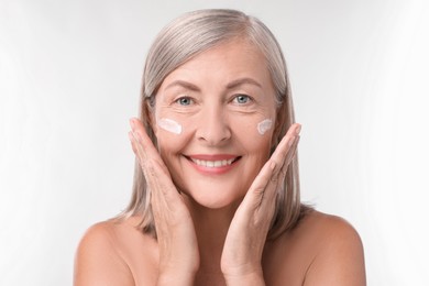 Photo of Senior woman with face cream on white background