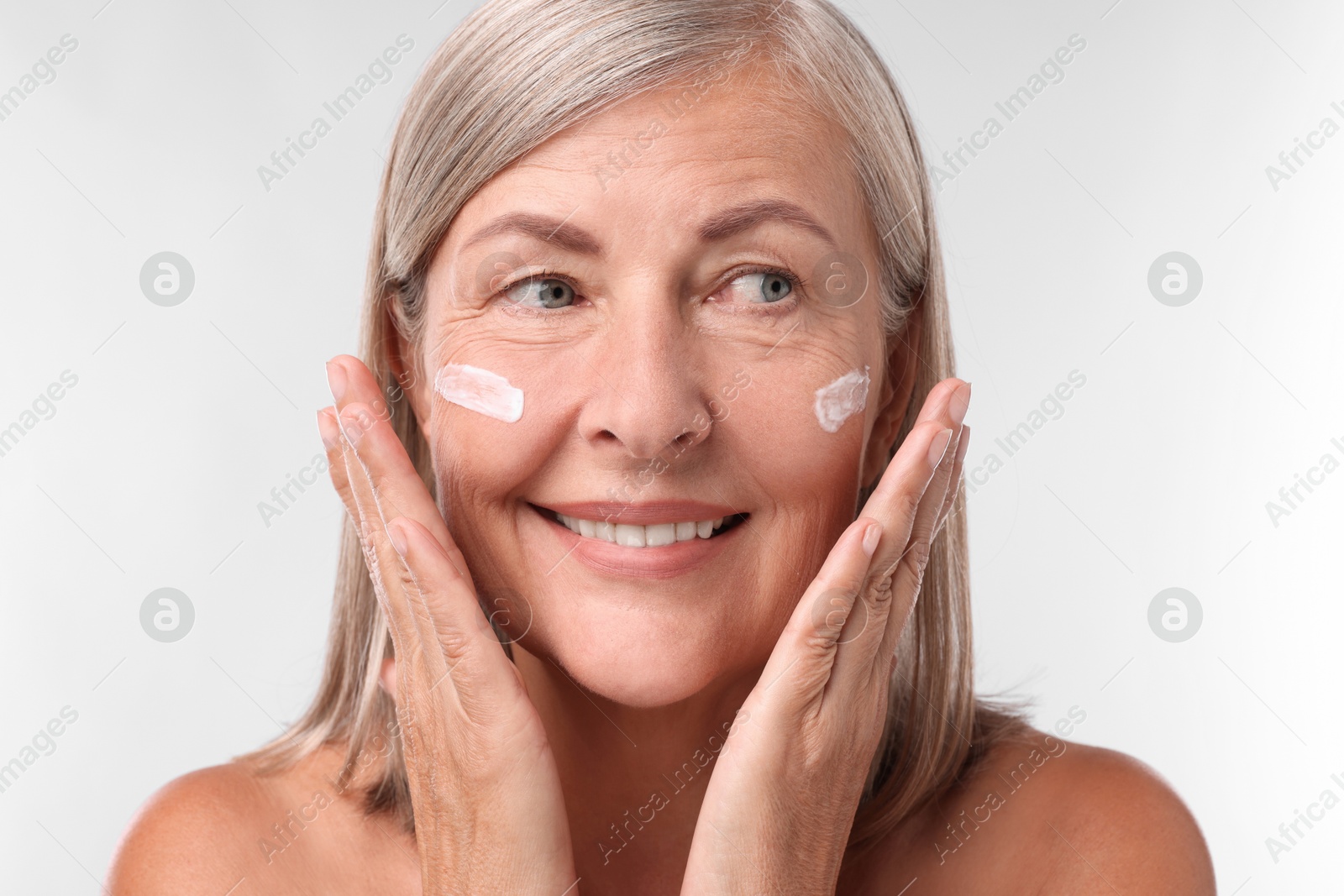 Photo of Senior woman with face cream on white background