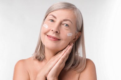 Photo of Senior woman with face cream on white background