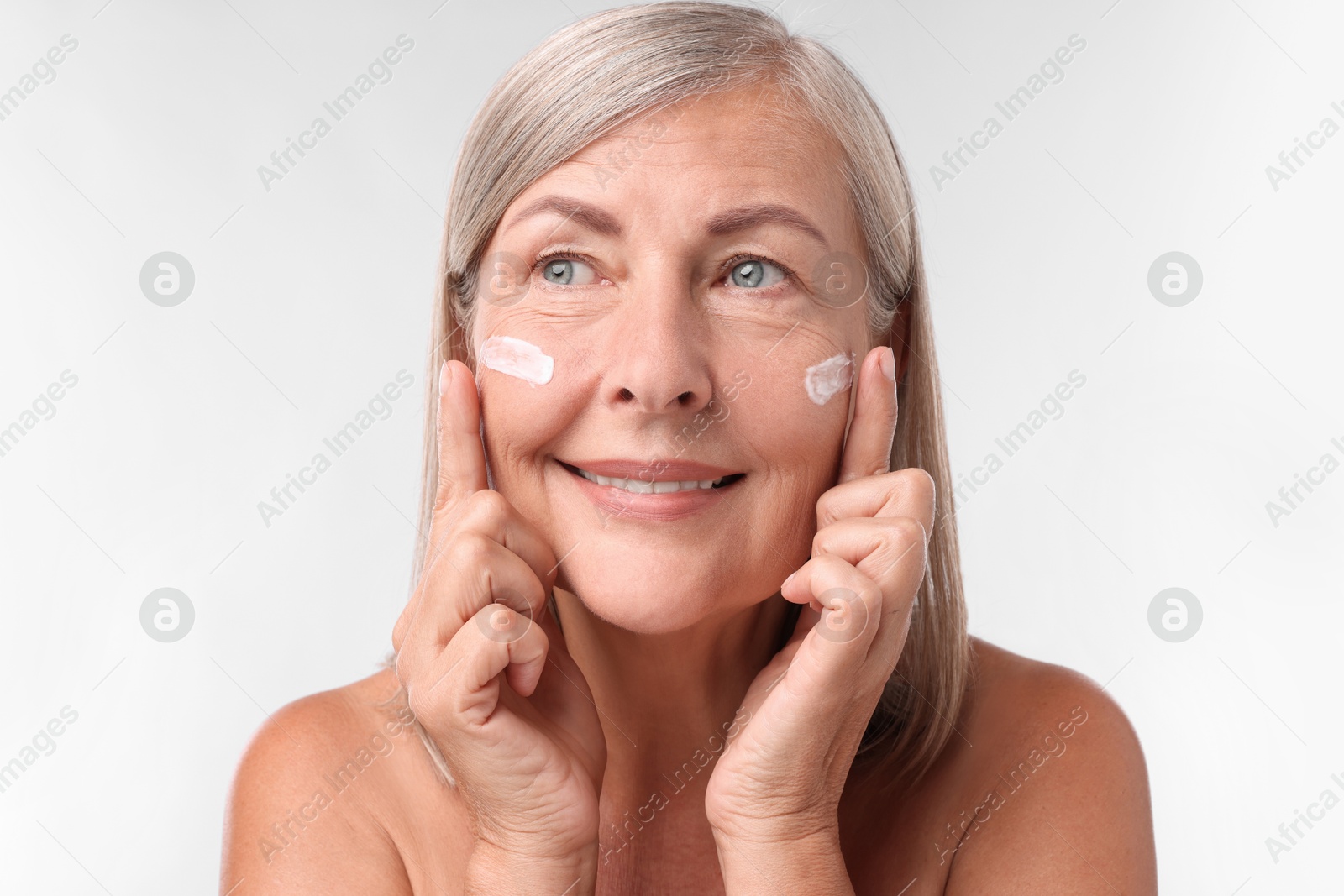 Photo of Senior woman with face cream on white background