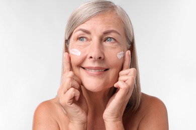 Senior woman with face cream on white background