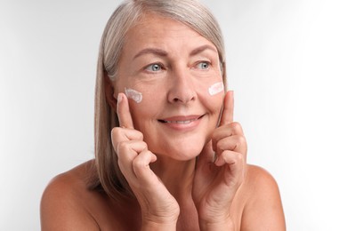 Senior woman with face cream on white background