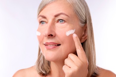 Senior woman applying face cream on white background