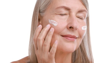 Photo of Senior woman applying face cream on white background, closeup