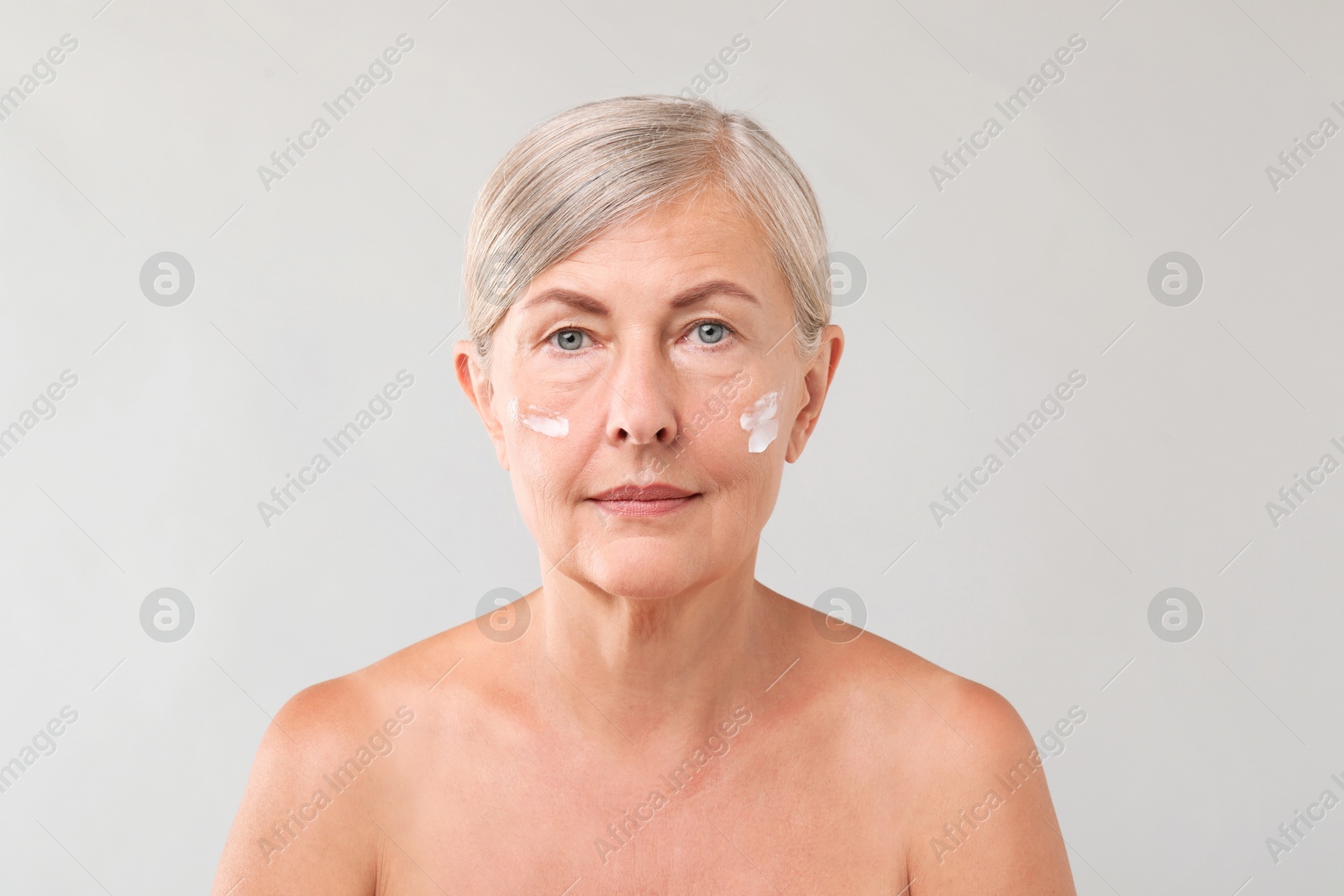 Photo of Senior woman with face cream on light background