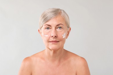 Senior woman with face cream on light background