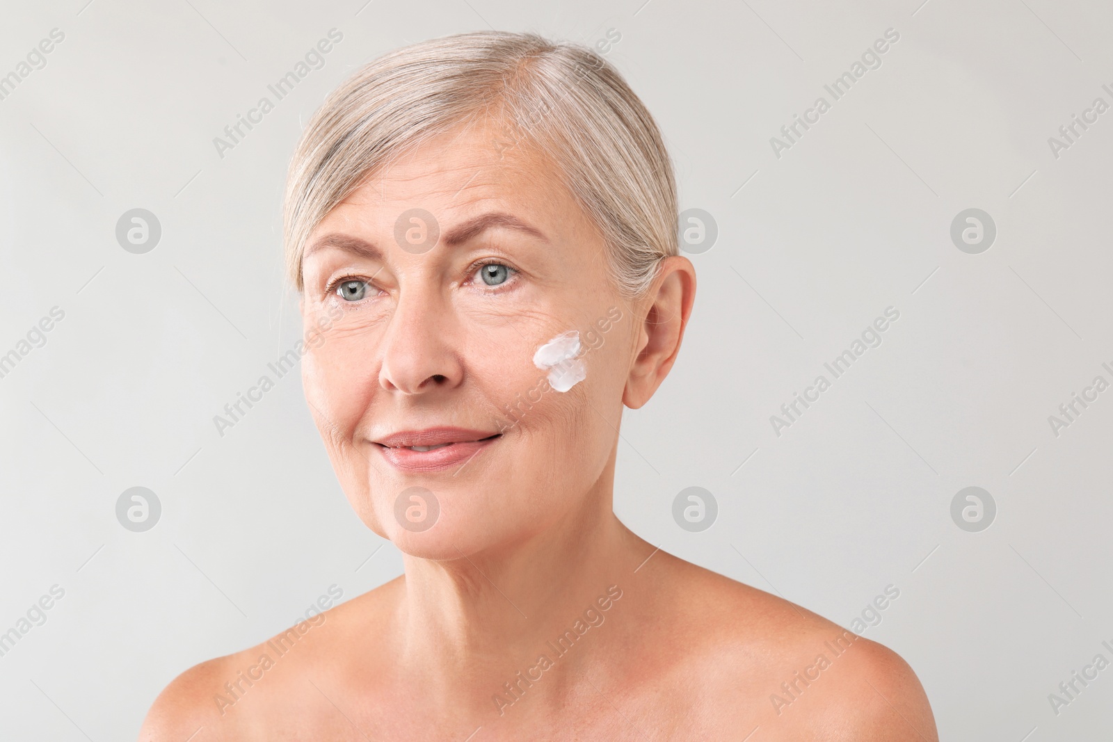 Photo of Senior woman with face cream on light background