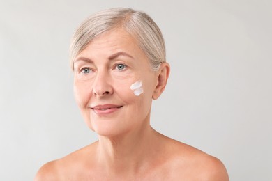 Senior woman with face cream on light background