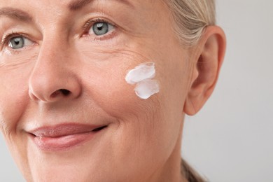 Photo of Senior woman with face cream on light background, closeup