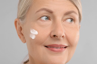 Senior woman with face cream on light background, closeup