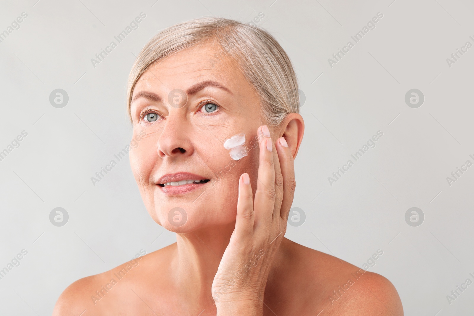 Photo of Senior woman applying face cream on light background