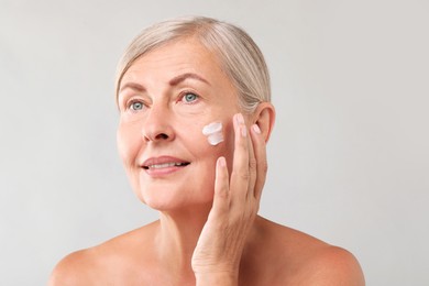 Senior woman applying face cream on light background