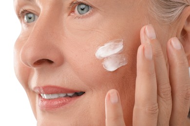 Senior woman applying face cream on light background, closeup