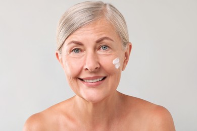 Senior woman with face cream on light background