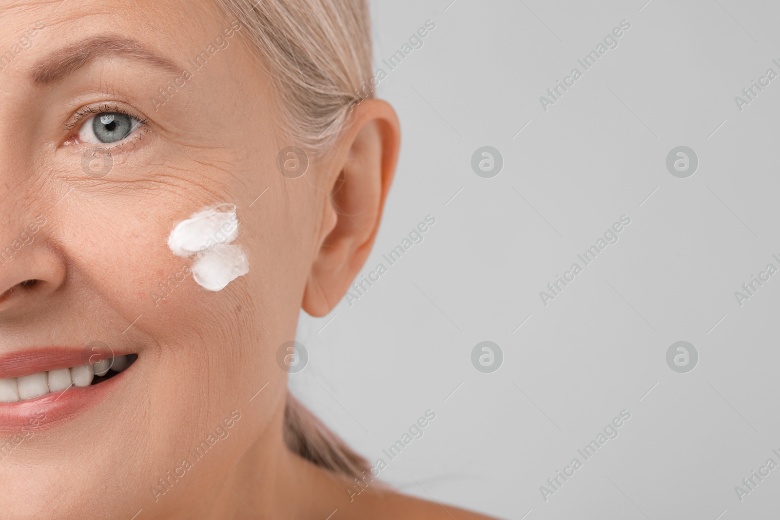 Photo of Senior woman with face cream on light background, closeup. Space for text