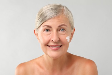 Senior woman with face cream on light background