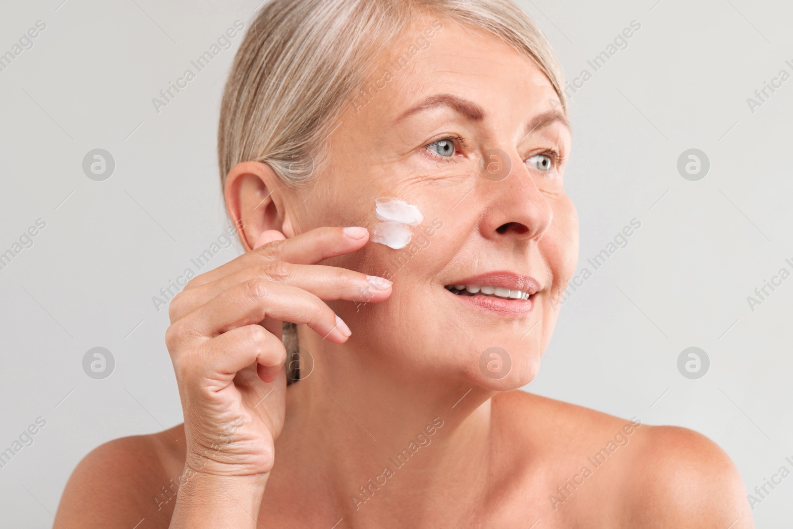 Photo of Senior woman with face cream on light background